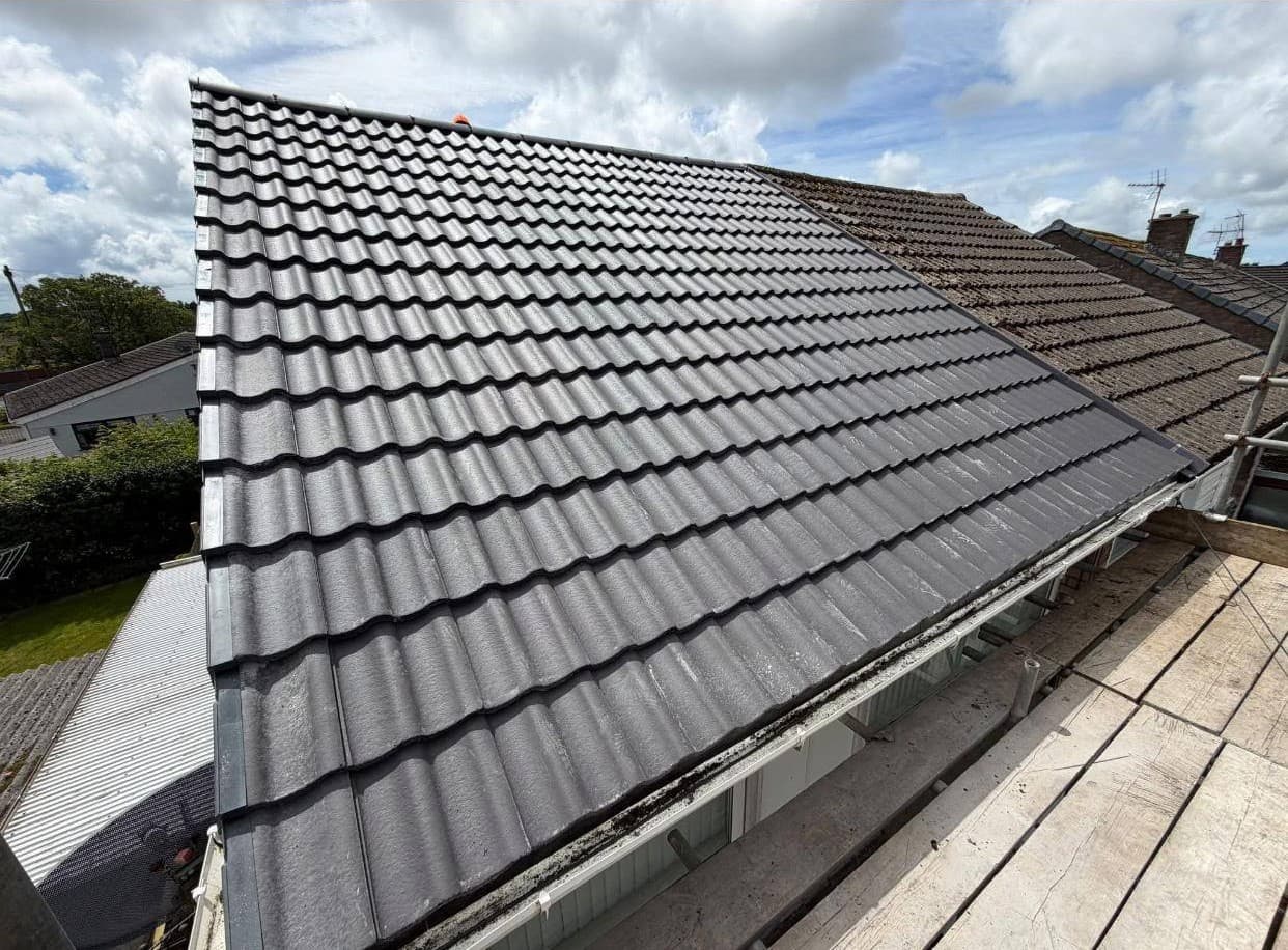 A completed reroof in new dark grey tiles, beside the original mossy roof of the house next door